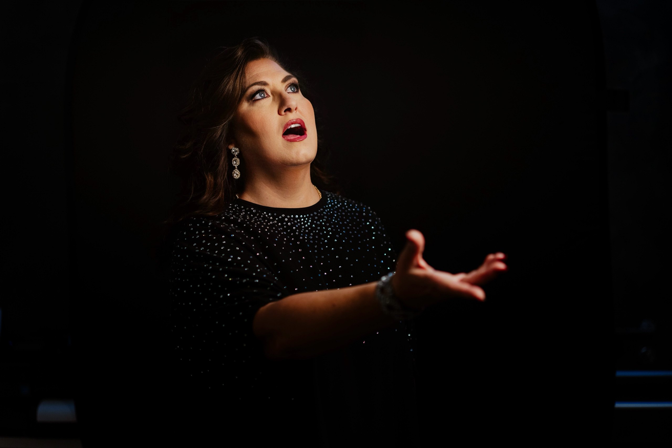 Il soprano Anna Pirozzi mentre canta con il braccio teso, su sfondo nero